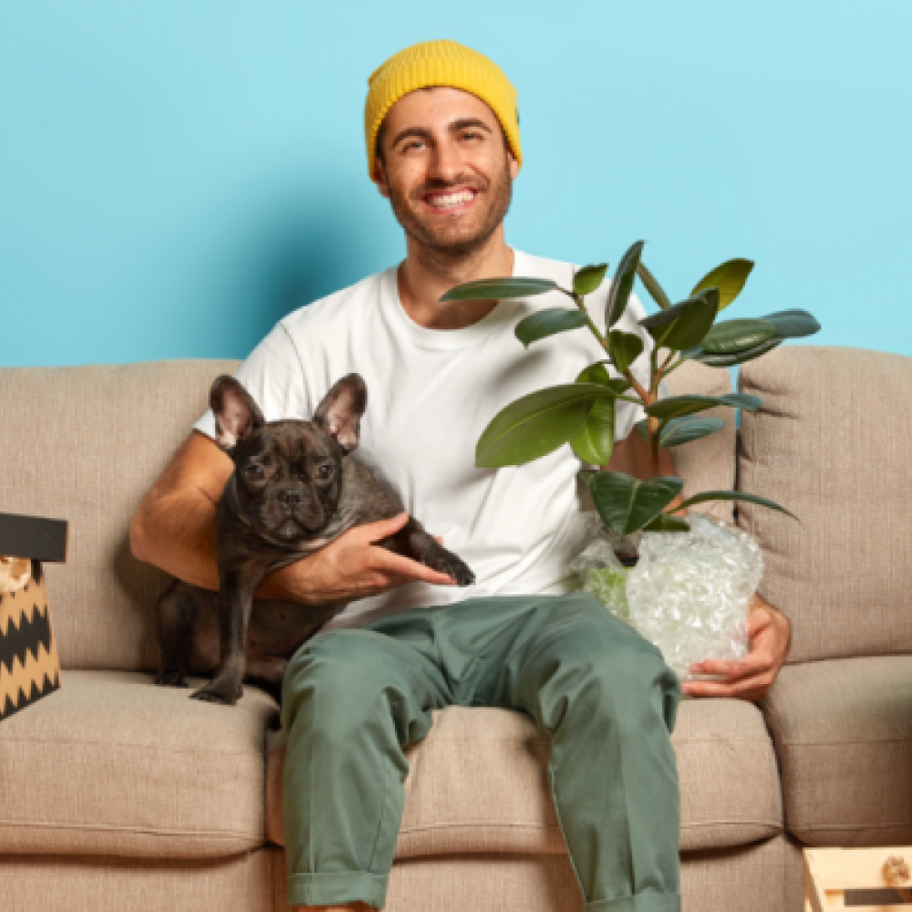 Man sitting on a couch with a dog and plant